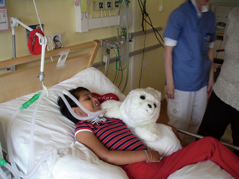 喉に呼吸器が繋がっている子供が病院のベッドでパロを抱いて喜んでいる写真
