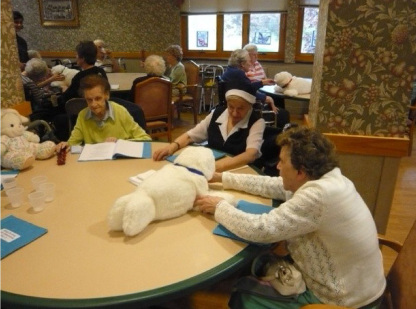 高齢者が数名椅子に座って丸テーブルを囲みテーブルの上のパロを見ている写真
