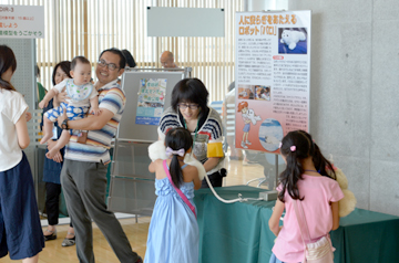 パロを手渡される子どもと、その横でパロを見つめる赤ちゃんを抱いた親子