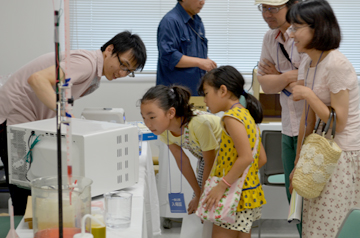 展示を熱心に見つめる子どもたちと、その後ろの大人