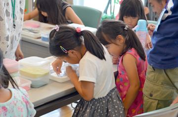 カラフルな材料の入った容器のそばで、浅い皿に向かって作業する子どもたち