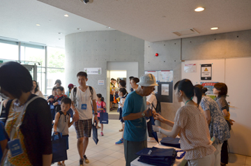 受付で来場者が資料袋を受け取っている様子