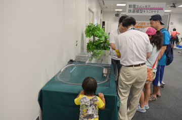 展示模型を囲んで説明を聞く来場者と、手前でのぞき込む子ども