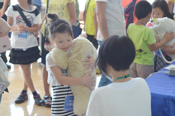 アザラシロボットのパロを抱えた子供としゃがんで目線を合わせて案内しているスタッフ