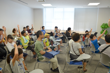 講義室で質問に手を挙げる子どもたちと大人たち