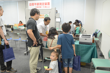 血管年齢測定の受付で、家族連れが案内を受けている様子