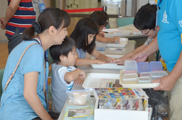 テーブルで子どもたちが材料を使って工作に取り組み、大人がサポートしている様子