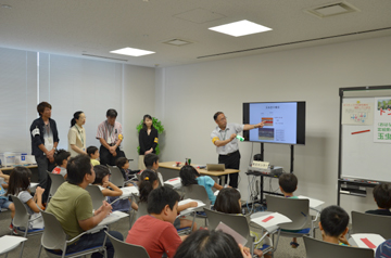 講義室でスタッフがスライドを使って説明し、参加者が席で聞いている様子