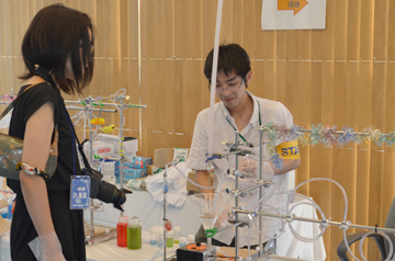 実験ブースでスタッフが装置について来場者に説明している様子