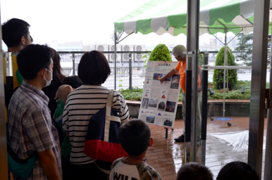 バルコニーのテント下でスタッフがパネルを使って来場者に説明している様子