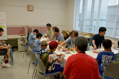 子どもたちがテーブルでスタッフから作業の説明を受けている様子