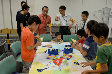 子どもたちがテーブルで工作を行い、スタッフが見守っている様子