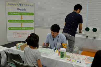 体験ブースで子どもが水流の実験を教わっている様子