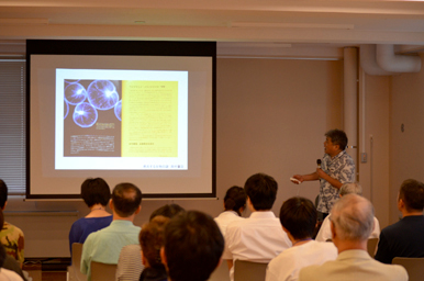 講師がスクリーンに映したスライドを指し示しながら聴衆に説明している様子