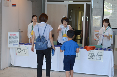 受付カウンターでスタッフから案内を受ける親子の様子