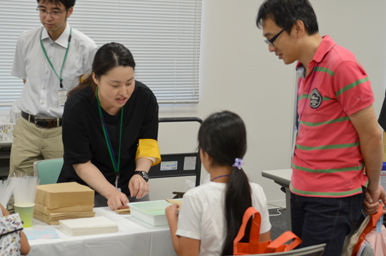 スタッフが机の上の材料を示しながら子どもに作業手順を説明している様子
