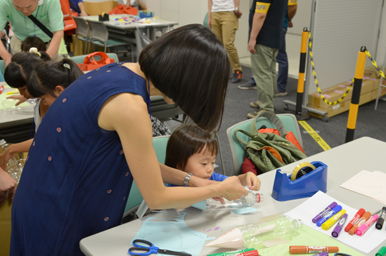 テーブルで工作に取り組む子どもに、大人が手を添えて教えている様子