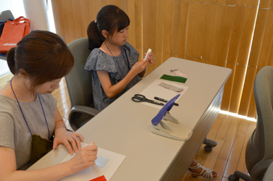 テーブルで子どもと大人が紙を使った工作に取り組んでいる様子