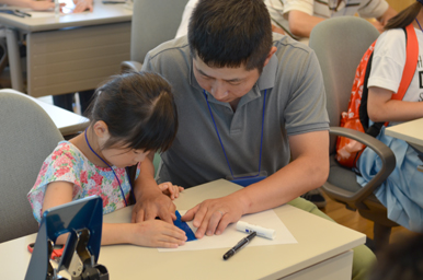 大人が子どもの手元に手を添えて、紙工作の作業を一緒に進めている様子