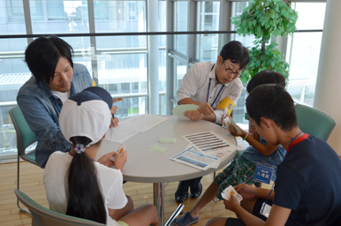 丸いテーブルを囲んで、スタッフが子どもたちに教材を使って説明している様子