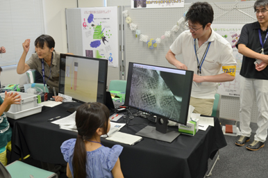 モニターに映る拡大映像を前に、スタッフが機器を操作し、子どもが観察している様子
