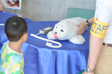 パロのロボットアザラシがテーブルに置かれ、子どもが興味深そうに見つめている様子