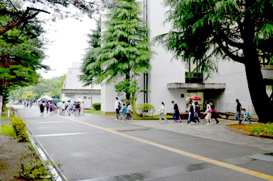 雨上がりのキャンパス通路を、多くの来場者が傘を持って歩いている様子