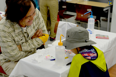 テーブルで実験材料を前に、大人と子どもが向かい合って作業している様子