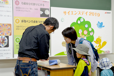 卓上の実験装置を使って、スタッフが親子に操作方法を教えている様子