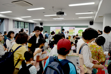 教室内の各ブースで多くの親子が体験活動に参加し、スタッフの説明を聞いているにぎやかな様子