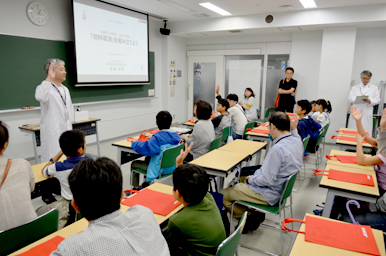 講師が教室前方で話をし、参加者の子どもたちが手を挙げて答えている様子