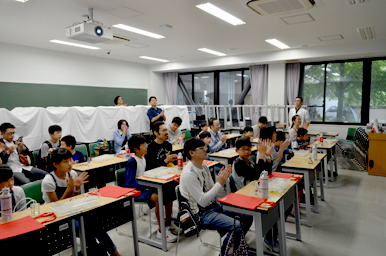 講義を終え、教室の子どもたちと大人が前方に向かって拍手している様子