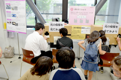 光の模様を見る装置の前で、子どもたちが座って観察し、スタッフがサポートしている様子