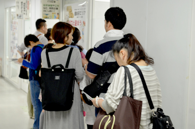 体験教室の前の廊下で、案内ポスターを見ながら順番を待つ来場者たち