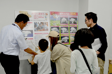 パロの説明パネルを前に、スタッフが指し示しながら親子に特徴を伝えている様子