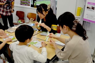 テーブルで紙工作の手順を教わりながら、親子が一緒に作業している様子