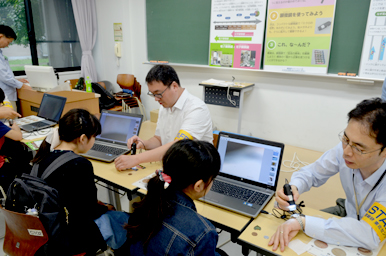 ノートパソコンに接続された顕微鏡を使って、来場者が試料を観察し、スタッフが操作をサポートしている様子