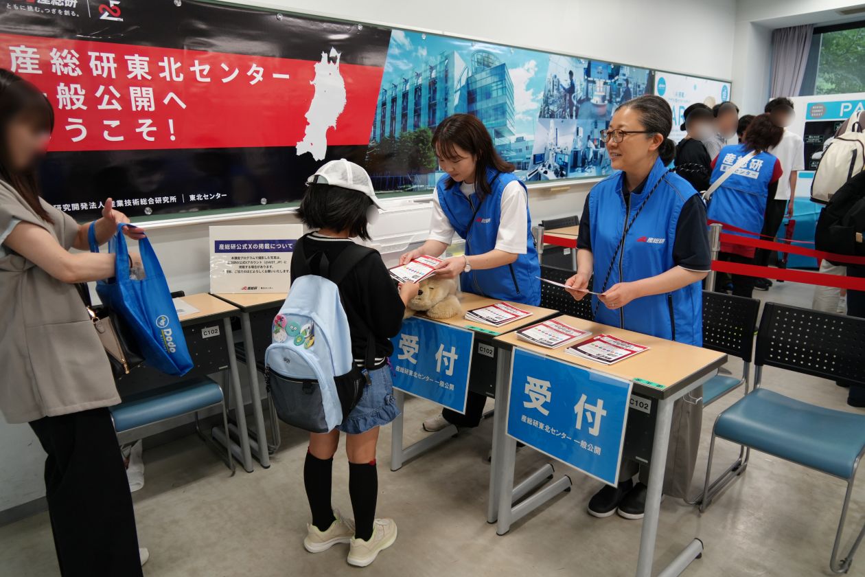 来場者が受付ブースでスタッフから資料配布と案内を受ける様子