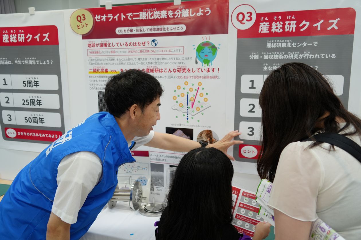 産総研クイズに挑戦する来場者にスタッフがヒントを説明している様子